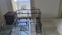 Multiple wire and wicker storage baskets and organizers on a flat surface, showing black, white, and silver metal baskets along with wicker baskets.