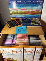 Photo showing Lyra Aquacolor 48-color pastel box, wooden drawers with soft pastels, pastel crayons and pencils, and artist pastel pads.