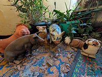 Wide view showing all seven pig garden statues together among plants and leaves on a woven surface.