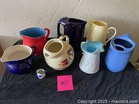 Overview of eight assorted pitchers of various colors and materials together on black surface