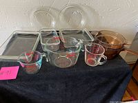 Overview of the entire set showing Pyrex and Vision Ware glass cookware including mixing bowls, measuring cups, square and rectangular baking dishes, and amber glass saucepan.