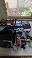 Wide shot of the entire lot on table including cameras, camcorder, film packs, camera cases, and chargers.