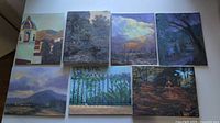 All seven acrylic landscape paintings laid out on a flat surface, showing variety in subject matter from architectural, natural, to garden scenes.