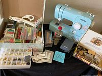 Wide view showing blue Brother sewing machine, thread spool organizer, Singer cutter, assorted tools, and button boxes.