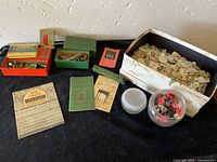 Photo showing full lot arranged on a table: boxes of Singer parts, sewing pins, instruction booklets, a large box with white buttons, and a glass bowl with assorted buttons.