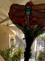 Close-up image of the dragonfly-themed stained glass shade and upper part of the lamp's metal stand.