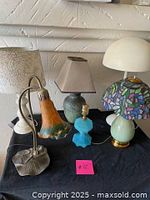Full view of all five lamps showing varied styles including frosted flower glass, floral fabric shade, blue glass base, white dome, and stained glass style shade with green ceramic base.