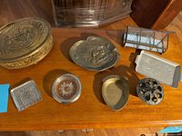 Various vintage decorative trays and dishes arranged on wooden table, showing main brass decorative tray and multiple smaller items.