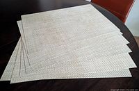 Stack of six beige/white vinyl basket-weave placemats on table