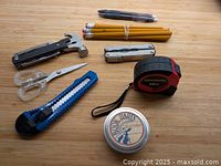 All items laid on wooden surface: Leatherman Fuse, Sheffield hammer multi-tool, utility knife, tape measure, Book Darts tin, scissors, pencils, pen