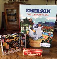 Front view showing signed hardcover book, Mini Lite-Brite box, harmonica box