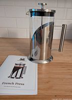 French press standing upright beside instruction booklet on countertop