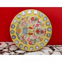 Front view of circular yellow embroidered artwork with attached coins on marble surface against red background