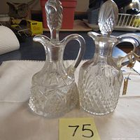 Two antique cut glass cruets together on a cloth background, showing full bodies and stoppers