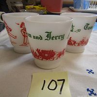 Three white milk glass Tom and Jerry eggnog mugs with red and green holiday designs grouped together.