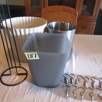 Image showing three waste bins including one beige ribbed plastic bin, one square matte grey bin, one shiny metal cylinder bin, a black metal toilet paper holder, and twelve silver metal shower curtain rings.