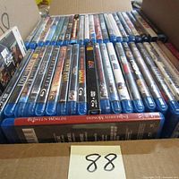 Photo of multiple Blu-ray movies in a cardboard box, showing spines of various films including 'Between Worlds'.