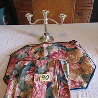 Photo showing metal three-arm candle holder and folded floral cloth placemat with item tag 190