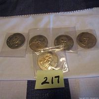 Five 1967 John Diefenbaker CBC broadcast memorial coins laid out on fabric surface.