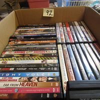 Photo showing a box filled with multiple DVD cases stacked and organized in rows. Titles include Olympus Has Fallen, Infinity, Collateral, among others.