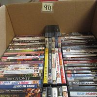 Photo showing the majority of DVD titles stacked in rows within a cardboard box, displaying titles such as Captain Phillips, Contagion, Beaches, and others.