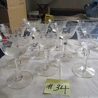 Group photo showing nine clear crystal glasses with etched floral patterns, arranged on a white cloth.