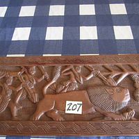 Close-up of the hand carved central scene showing human figures and large horned animal with detailed facial expressions and sport-like poses.