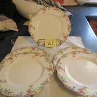 Five salad plates with floral border pattern and gold rim, arranged on table with one standing on a holder