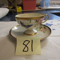 Teacup on matching saucer showing floral and butterfly handpainting and gold trim