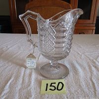 Front view of antique clear pressed glass cream pitcher with Jacob's Ladder pattern, showing detailed diamond and rectangular textures, angular handle, and wide pouring spout.
