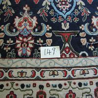 Close-up of rug pattern showing floral and urn motifs on navy background