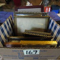 Photo of the box containing 14 assorted picture frames in various sizes and conditions showing multiple frame edges and styles stacked
