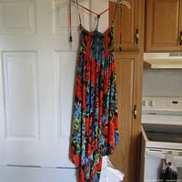 Full length view of the colourful strapless summer dress hanging on hanger against white door and kitchen background.