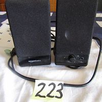 Front view of two black AmazonBasics computer speakers on white cloth with mesh fronts and cables visible.