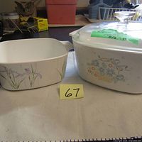 Two Corningware casserole dishes side by side; one with floral basket pattern and glass lid, other with purple flower decoration without lid.