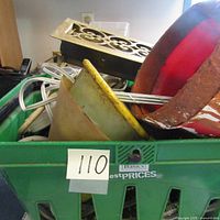 Green plastic carrier filled with various garage items including plastic funnels, a metal grate, and an old plastic bucket.
