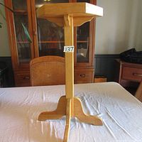 Front view of the solid wood plant stand showing the square top and tripod base on a white cloth surface.