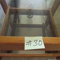 Top view showing clear glass top set within handmade solid wood frame, partial view of mirrored bottom shelf underneath.