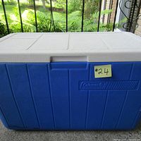 Front view of a large blue Coleman cooler with white textured lid and Coleman branding visible.