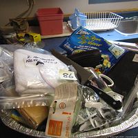 Shows a variety of unopened household items including Ziploc bags, kitchen knives, a package of never used white textiles, and disposable ponchos.