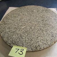 Top-down view of round marble lazy Susan showing full shape and speckled granite-like surface with a sticker number 73.
