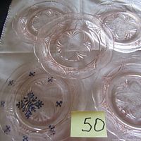 Five translucent pink Depression glass small plates arranged on a cloth background with a paper note showing number 50.