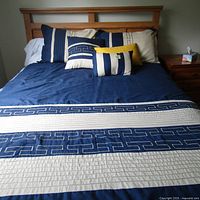 View of queen size bed with blue and beige comforter with geometric Greek key patterns and three decorative pillows arranged on the bed.