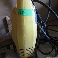 Close-up of top and side of yellow electric pressure washer showing scuff marks, power cord coiled beside unit.