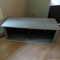 Full view of gray TV stand showing flat rectangular top surface and two open shelving compartments below.