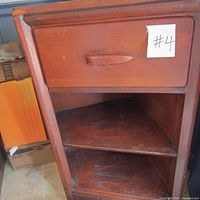 Front view of the corner shelf showing triangular shape, single drawer with wooden handle, and two open shelves below.