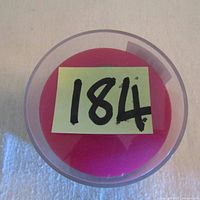 Top view of the round pink base of the packaged speaker with auction lot number 184 on sticky note.