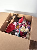 Box containing multiple Barbie dolls and various doll-sized clothing and accessories shown from above.