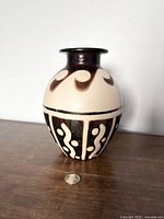 Front view of Chulucanas pottery vase with visible black and cream patterns and coin for scale.