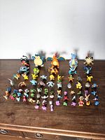 Wide view showing full collection of 56 mixed Pokémon figures arranged in rows on a wooden surface against a white background.